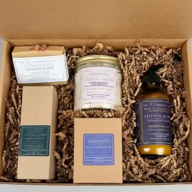 Box with bath and body products including a candle, soap, and bottle on a green surface.