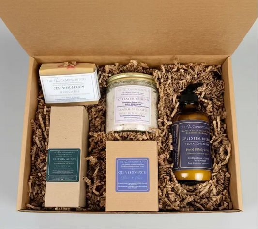 Box with bath and body products including a candle, soap, and bottle on a green surface.